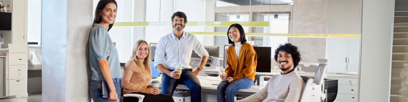 A diverse workplace team smiling together in a modern office, representing mental health support and positive workplace culture
